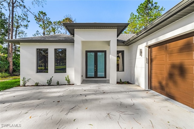 2717 10th Ave SE, Naples, FL 34117 - view of exterior entry with roof with shingles, french doors, stucco siding, an attached garage, and concrete driveway