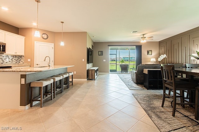 3943 E Hampton Cir, Alva, FL 33920 - kitchen featuring stainless steel microwave, tasteful backsplash, white cabinetry, light tile patterned floors, and light stone counters