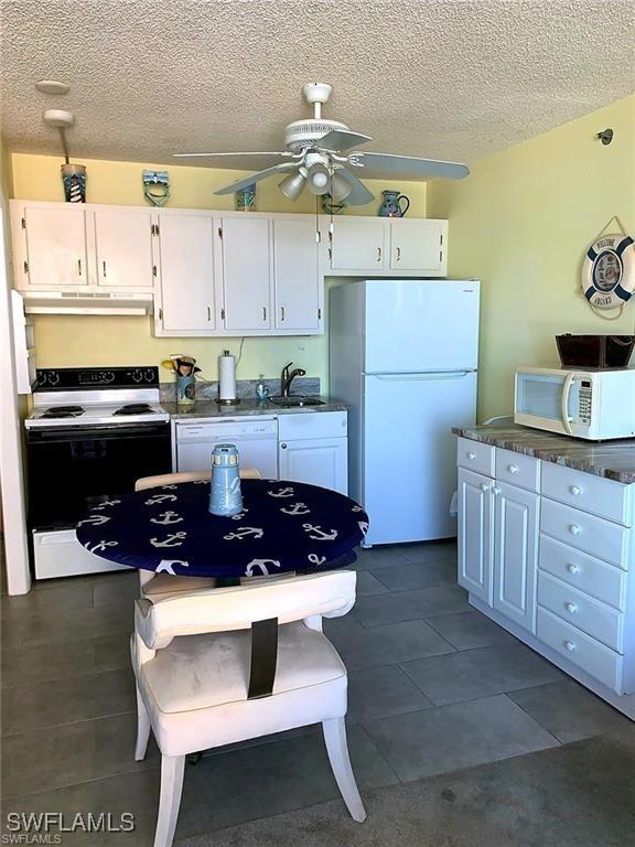 8701 Estero Blvd Unit 605, Bonita Springs, FL 33931 - kitchen featuring white appliances, under cabinet range hood, ceiling fan, white cabinetry, and dark countertops