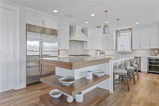 434 Trade Winds Ave, Naples, FL 34108 - kitchen with stainless steel built in fridge, custom range hood, wine cooler, white cabinets, and recessed lighting