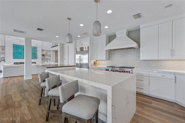 434 Trade Winds Ave, Naples, FL 34108 - kitchen with custom range hood, a center island, white cabinetry, wood finished floors, and light stone counters