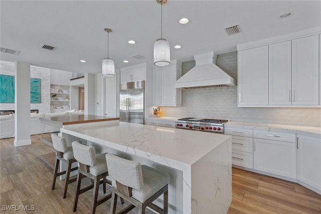 434 Trade Winds Ave, Naples, FL 34108 - kitchen featuring custom exhaust hood, white cabinets, light wood-type flooring, a center island, and open floor plan