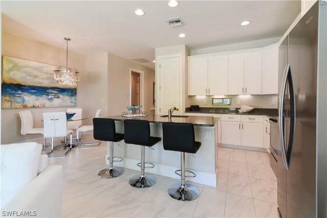 kitchen featuring stainless steel fridge, pendant lighting, white cabinets, and a kitchen island with sink