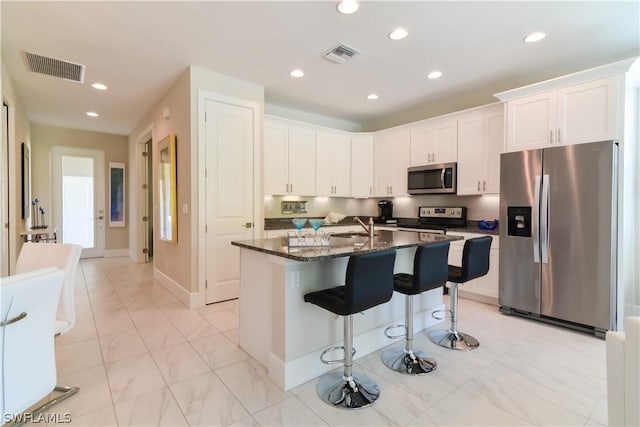 kitchen with a kitchen breakfast bar, stainless steel appliances, dark stone countertops, white cabinets, and light tile floors