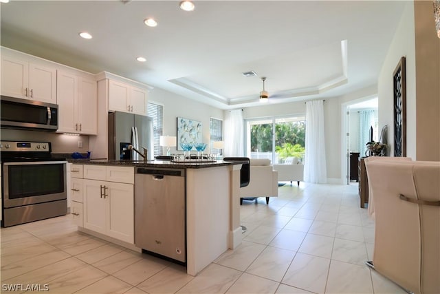 kitchen with white cabinets, appliances with stainless steel finishes, a tray ceiling, and dark stone countertops