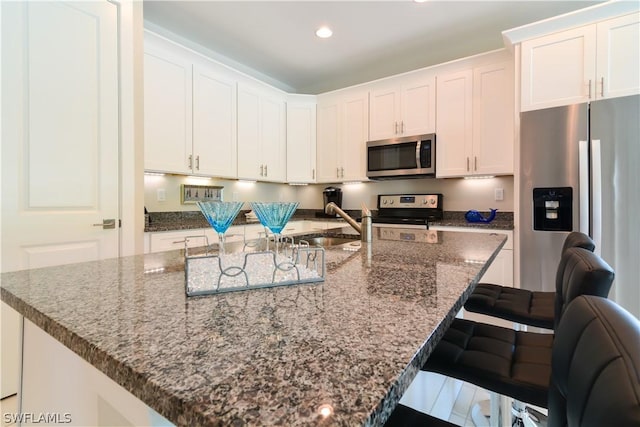 kitchen with an island with sink, dark stone counters, a kitchen breakfast bar, white cabinets, and appliances with stainless steel finishes