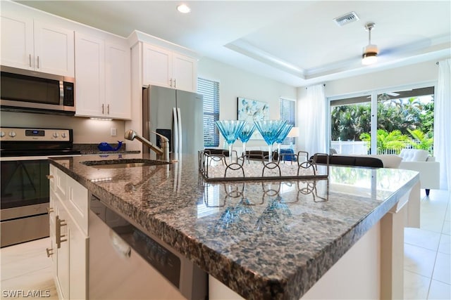 kitchen with white cabinetry, a kitchen island with sink, appliances with stainless steel finishes, sink, and light tile floors