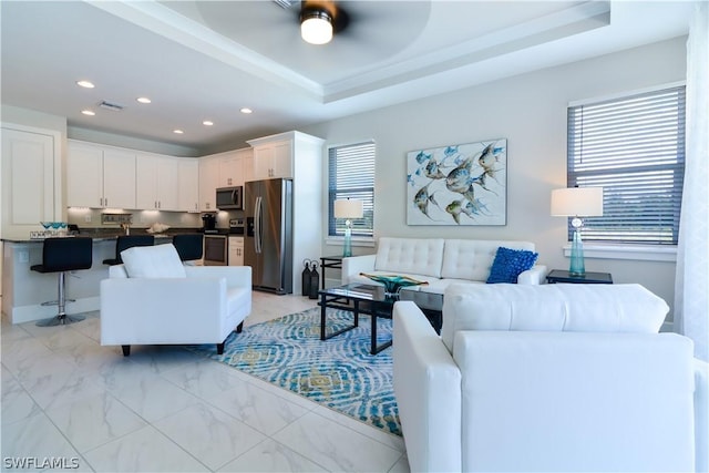 tiled living room with a raised ceiling, ceiling fan, and a wealth of natural light