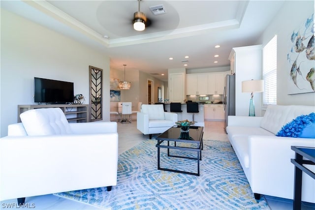 tiled living room featuring ceiling fan with notable chandelier and a raised ceiling