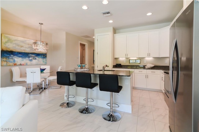 kitchen featuring white cabinets, an island with sink, hanging light fixtures, and stainless steel refrigerator