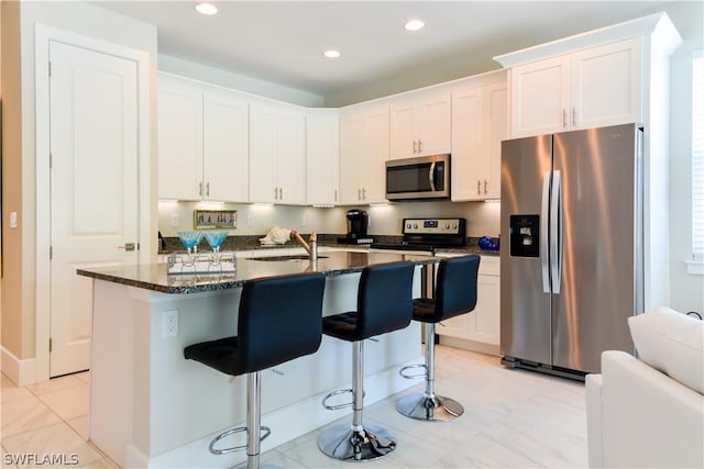 kitchen with light tile flooring, a center island with sink, a breakfast bar area, appliances with stainless steel finishes, and white cabinets