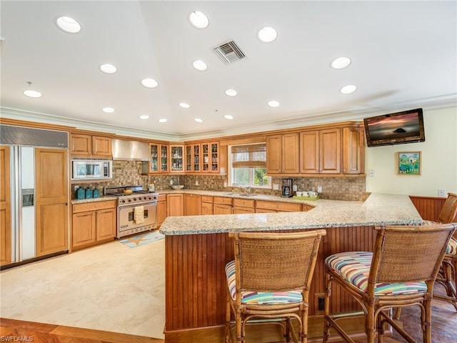 kitchen featuring kitchen peninsula, built in appliances, light tile flooring, and a breakfast bar