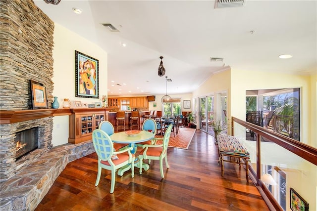 dining room featuring dark hardwood / wood-style flooring, vaulted ceiling, and a stone fireplace