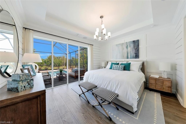 bedroom with a raised ceiling, access to exterior, a notable chandelier, and wood-type flooring