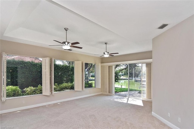 interior space with plenty of natural light, light colored carpet, ceiling fan, and a raised ceiling