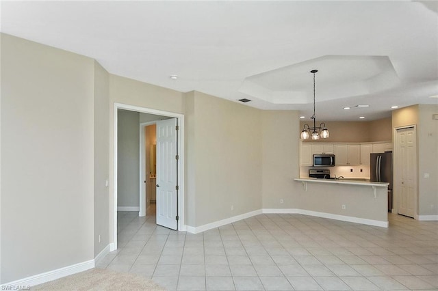 spare room featuring a chandelier, a tray ceiling, and light tile flooring