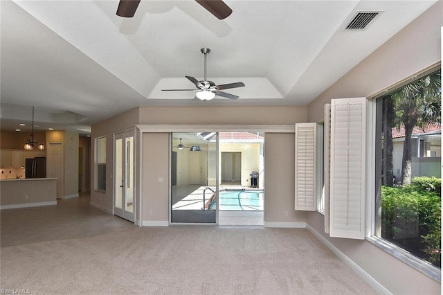 interior space with light colored carpet, ceiling fan, a tray ceiling, and a wealth of natural light