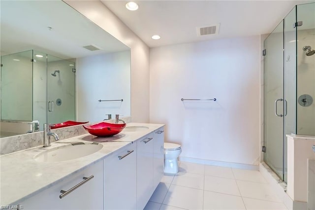 bathroom featuring double sink vanity, toilet, a shower with door, and tile flooring