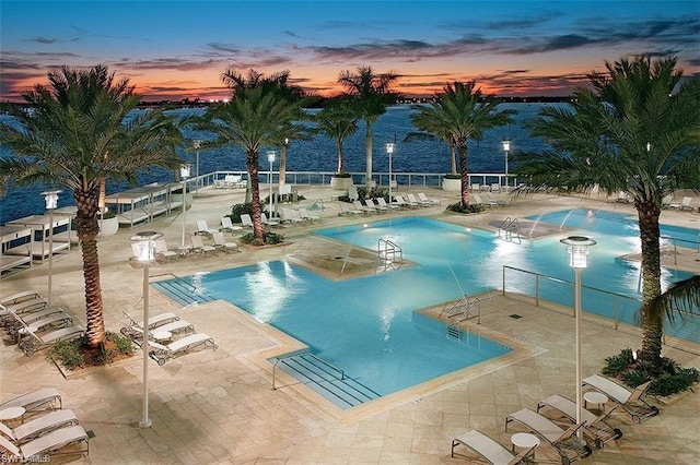 pool at dusk with pool water feature and a patio area