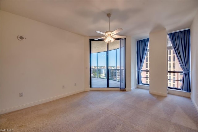 empty room featuring light colored carpet, ceiling fan, and expansive windows