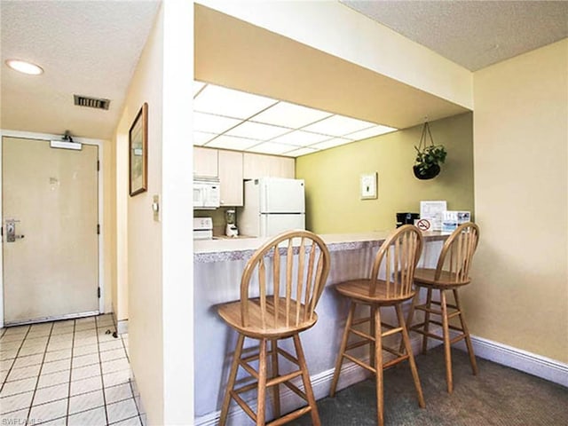 kitchen featuring white appliances, kitchen peninsula, a kitchen breakfast bar, and light tile flooring