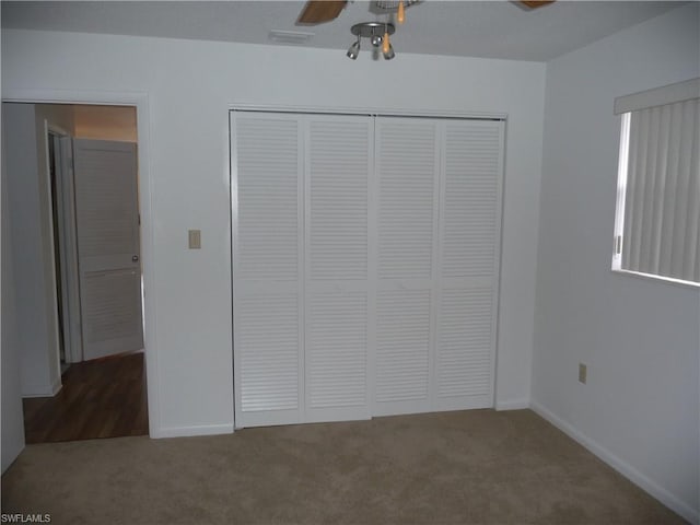 unfurnished bedroom with a closet, dark colored carpet, and ceiling fan