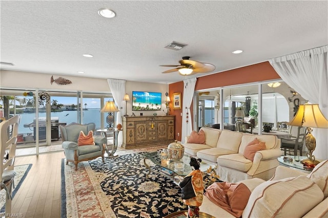 living room featuring a textured ceiling, light hardwood / wood-style floors, ceiling fan, and a water view