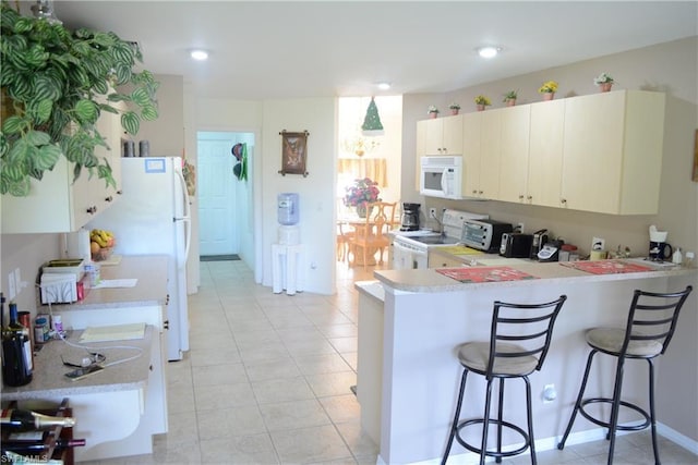 kitchen featuring light tile floors, kitchen peninsula, white appliances, a breakfast bar area, and white cabinets