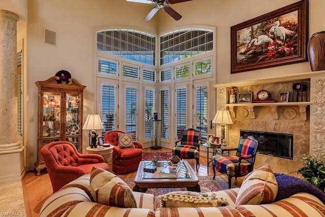 living room featuring ceiling fan, a high ceiling, a high end fireplace, light wood-type flooring, and ornate columns