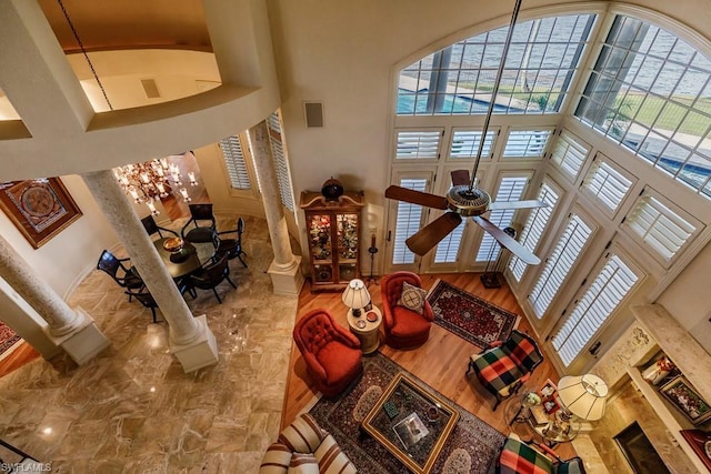 tiled living room featuring decorative columns, ceiling fan with notable chandelier, and a towering ceiling