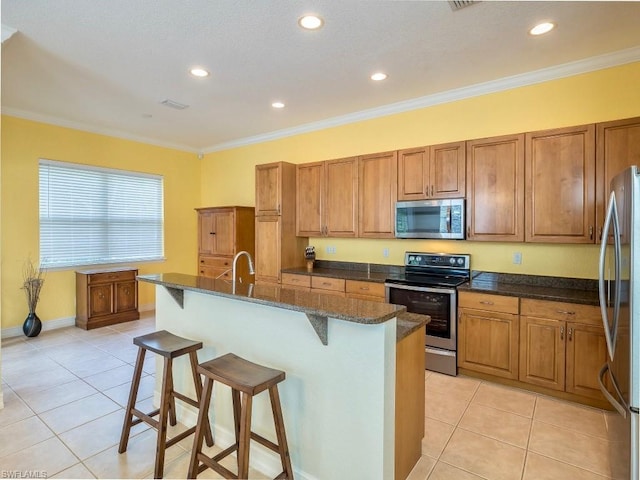 kitchen with an island with sink, crown molding, a kitchen breakfast bar, appliances with stainless steel finishes, and light tile flooring