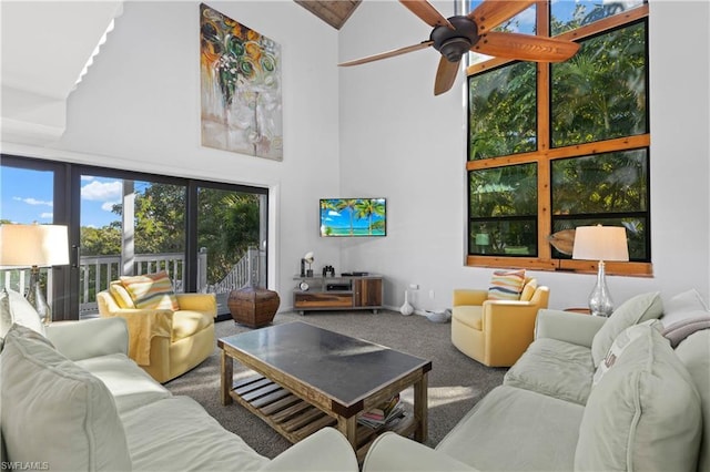 living room featuring ceiling fan, dark carpet, and a towering ceiling