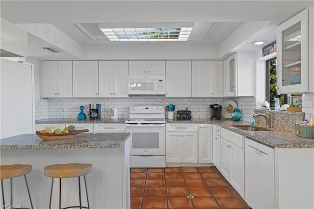 kitchen featuring white appliances, dark tile flooring, a kitchen breakfast bar, tasteful backsplash, and white cabinetry