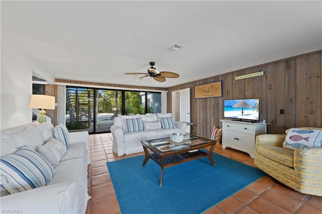 living room featuring wood walls, tile floors, and ceiling fan