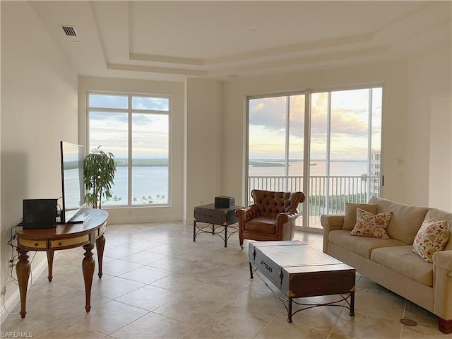 tiled living room featuring a water view and a tray ceiling