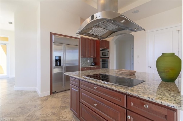 kitchen with backsplash, appliances with stainless steel finishes, light tile floors, light stone counters, and island range hood