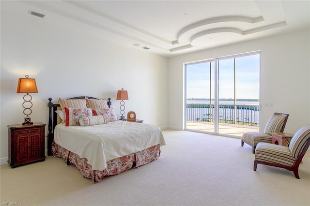 carpeted bedroom with a water view, a raised ceiling, and access to outside