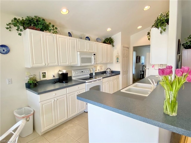 kitchen with light tile floors, kitchen peninsula, white appliances, white cabinetry, and sink