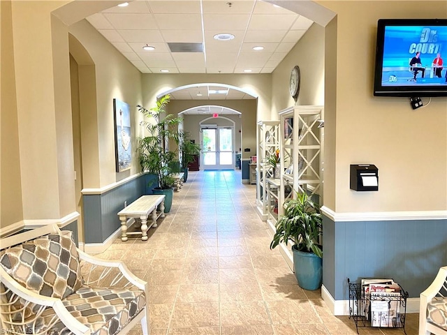 hallway with french doors, light tile flooring, and a drop ceiling