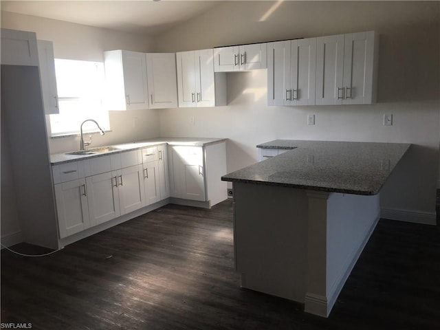 kitchen with dark stone countertops, white cabinetry, dark wood-type flooring, and sink