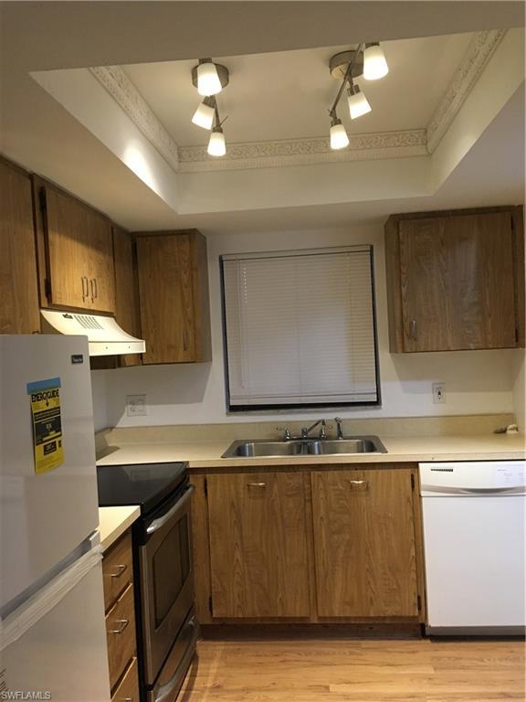 kitchen with white appliances, sink, a raised ceiling, rail lighting, and light hardwood / wood-style floors