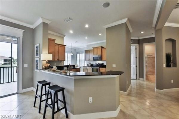 kitchen featuring light tile floors, stove, kitchen peninsula, a breakfast bar, and ornamental molding