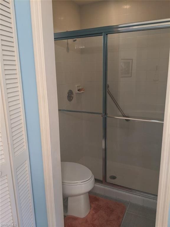 bathroom featuring toilet, tile flooring, and a shower with shower door