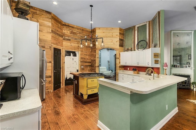 kitchen with kitchen peninsula, white cabinetry, stainless steel appliances, wood walls, and pendant lighting