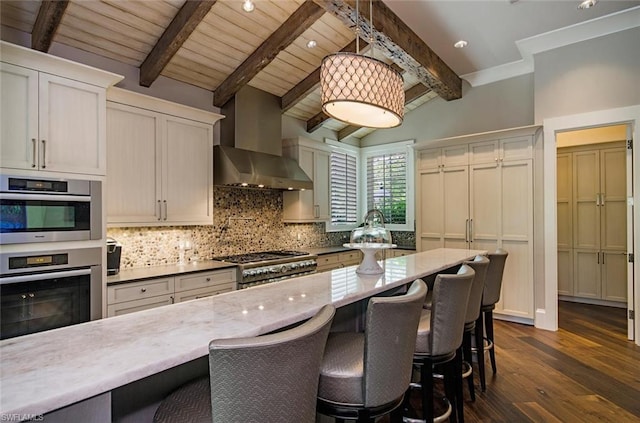 kitchen with a breakfast bar, double oven, wall chimney range hood, decorative light fixtures, and white cabinetry