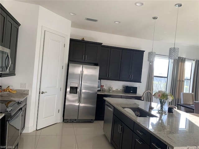 kitchen featuring pendant lighting, stainless steel appliances, sink, and light stone counters