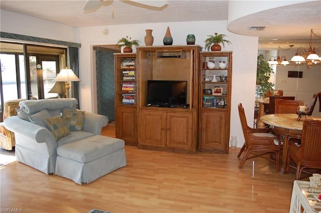 living room featuring a textured ceiling, ceiling fan with notable chandelier, and light wood-type flooring