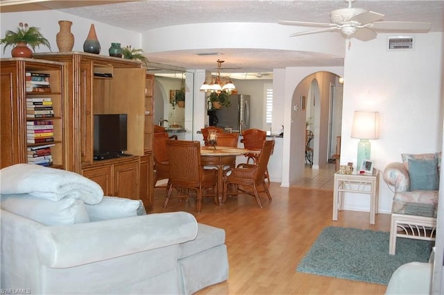 living room with a textured ceiling, light hardwood / wood-style floors, and ceiling fan with notable chandelier