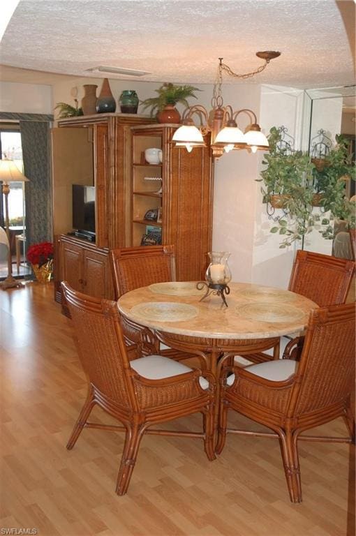 dining room featuring a textured ceiling, a chandelier, and light hardwood / wood-style floors