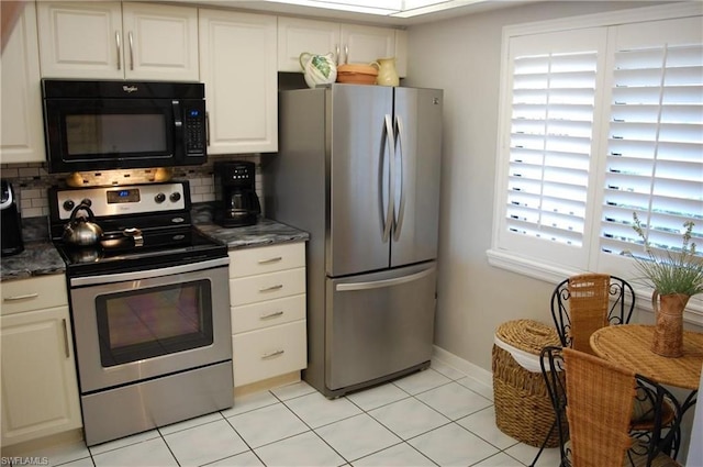 kitchen featuring white cabinetry, appliances with stainless steel finishes, light tile floors, dark stone countertops, and tasteful backsplash